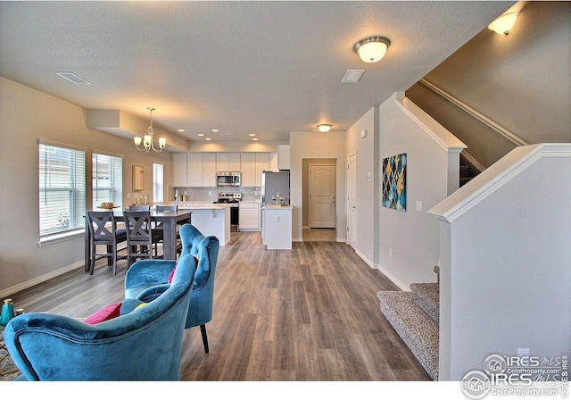 living room with stairway, wood finished floors, visible vents, baseboards, and a chandelier