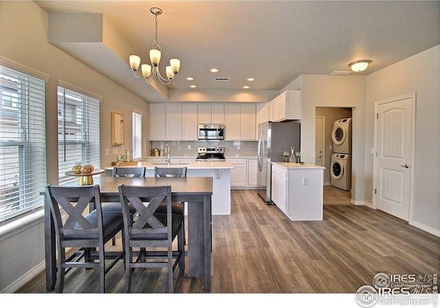 kitchen featuring stacked washer and dryer, stainless steel appliances, baseboards, a notable chandelier, and light countertops