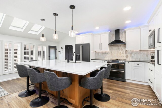 kitchen featuring wood finished floors, wall chimney range hood, a sink, decorative backsplash, and black appliances