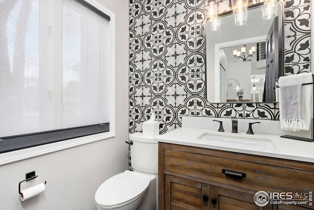 half bath with toilet, vanity, and an inviting chandelier