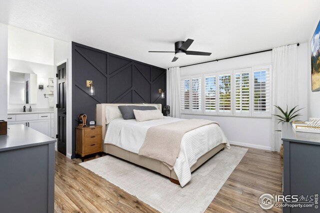 bedroom featuring light wood-style floors, ensuite bath, a ceiling fan, and baseboards