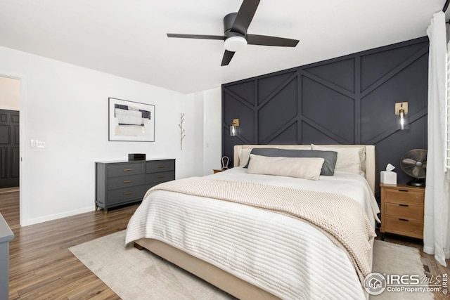 bedroom featuring ceiling fan, a decorative wall, wood finished floors, and baseboards
