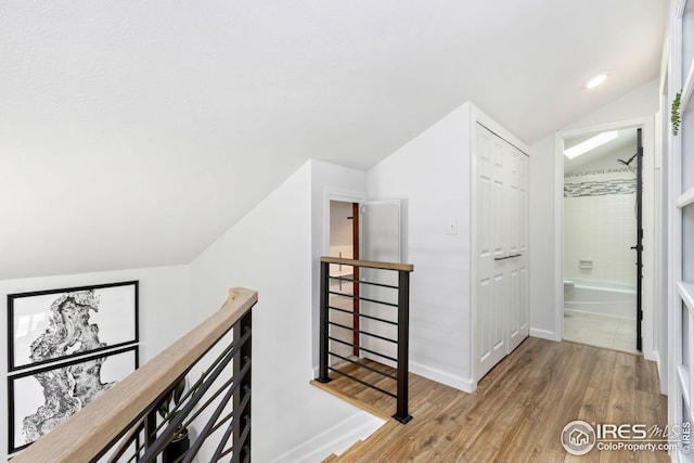 hall with vaulted ceiling, wood finished floors, an upstairs landing, and baseboards