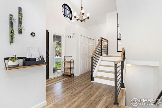 stairway with a high ceiling, baseboards, wood finished floors, and an inviting chandelier