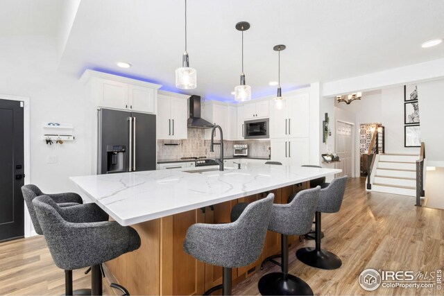 kitchen featuring wall chimney range hood, white cabinets, decorative backsplash, high quality fridge, and stainless steel microwave