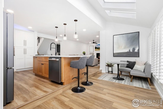kitchen with light wood-style flooring, light countertops, open floor plan, dishwasher, and an island with sink