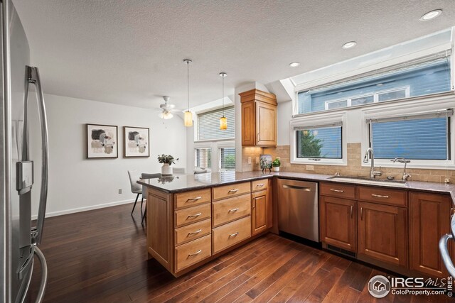 kitchen with a peninsula, a sink, appliances with stainless steel finishes, and dark wood finished floors