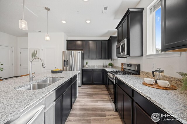 kitchen featuring visible vents, a sink, light stone countertops, hanging light fixtures, and appliances with stainless steel finishes
