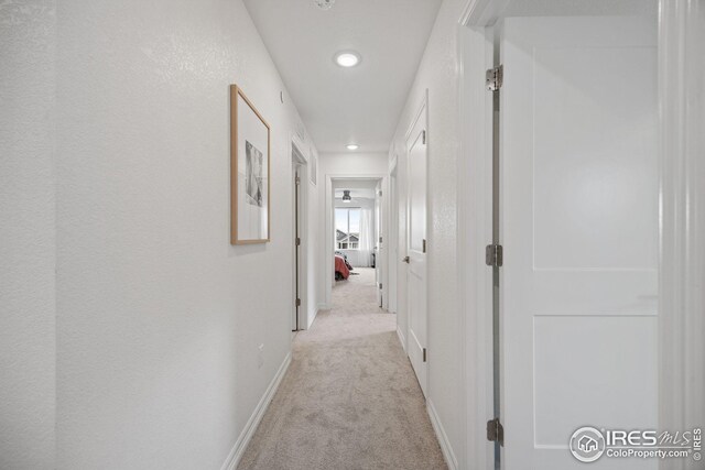 hallway with recessed lighting, baseboards, and light colored carpet