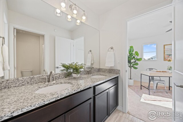 bathroom with toilet, a sink, double vanity, and baseboards