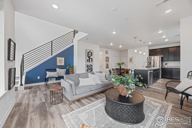 living room with light wood finished floors, visible vents, recessed lighting, and stairway