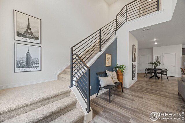 stairs featuring wood finished floors, a towering ceiling, baseboards, visible vents, and recessed lighting
