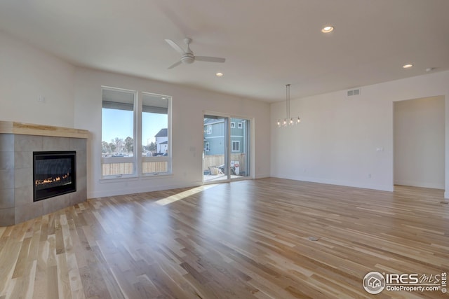 unfurnished living room featuring recessed lighting, a tile fireplace, ceiling fan with notable chandelier, light wood finished floors, and visible vents