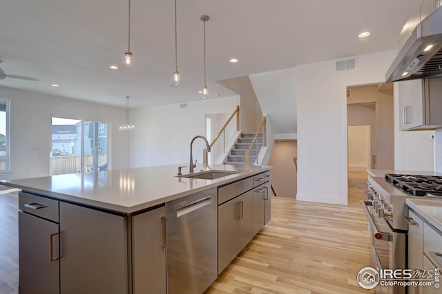 kitchen with a sink, under cabinet range hood, light wood-style floors, stainless steel appliances, and visible vents