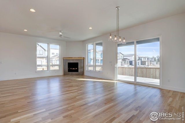 unfurnished living room with a wealth of natural light, a ceiling fan, light wood-style flooring, and baseboards