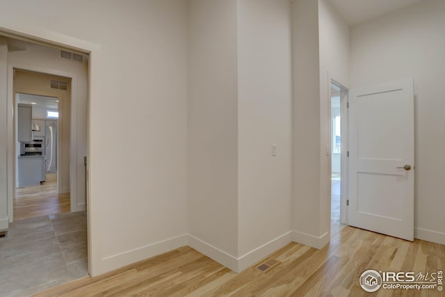 hallway with baseboards, visible vents, and light wood-style floors