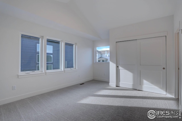 unfurnished bedroom with carpet, a closet, lofted ceiling, and baseboards
