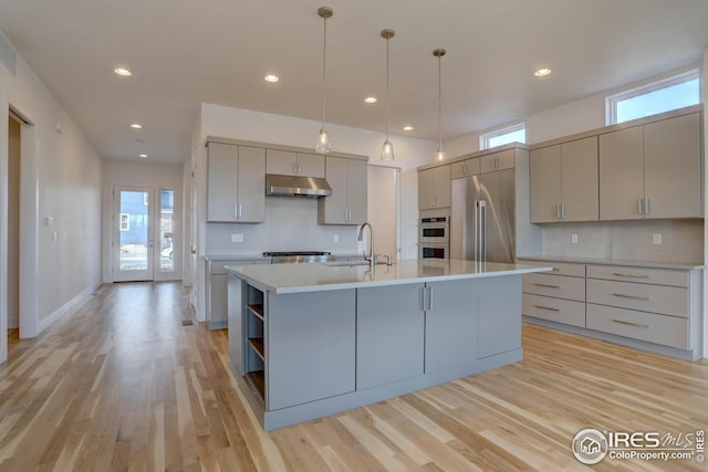 kitchen with a sink, appliances with stainless steel finishes, light countertops, under cabinet range hood, and backsplash