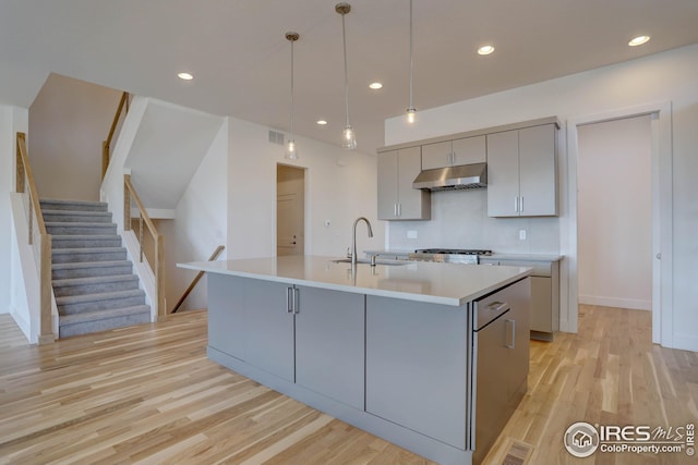 kitchen featuring a sink, light wood-style floors, light countertops, under cabinet range hood, and gray cabinets