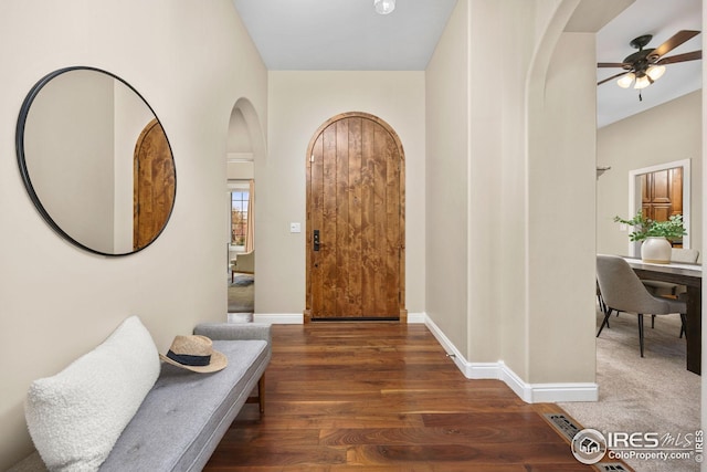 foyer with arched walkways, a ceiling fan, wood finished floors, and baseboards