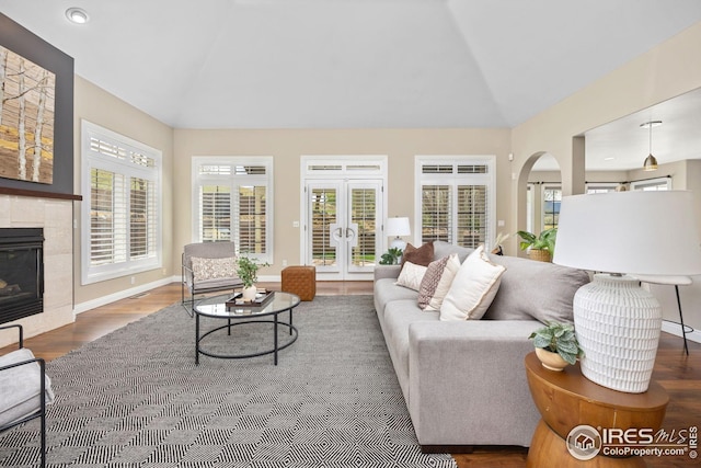 living room featuring wood finished floors, plenty of natural light, a glass covered fireplace, french doors, and lofted ceiling