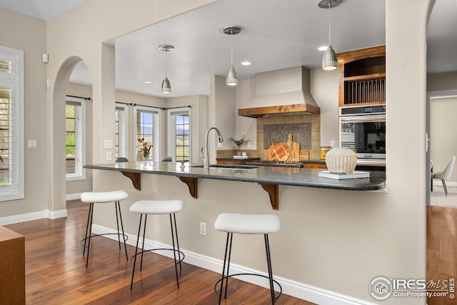 kitchen with custom exhaust hood, a sink, oven, arched walkways, and dark wood-style flooring