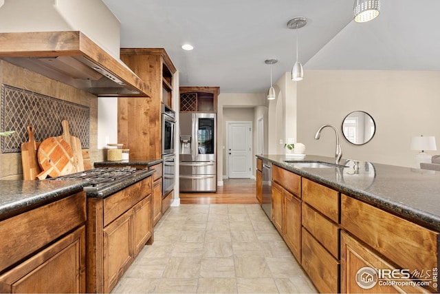 kitchen featuring brown cabinets, a sink, decorative light fixtures, wall chimney exhaust hood, and appliances with stainless steel finishes