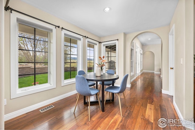 dining room featuring arched walkways, baseboards, visible vents, and dark wood-style floors