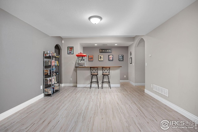 bar featuring arched walkways, wood finished floors, visible vents, and a bar