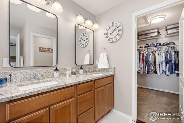 bathroom with a walk in closet, double vanity, baseboards, and a sink
