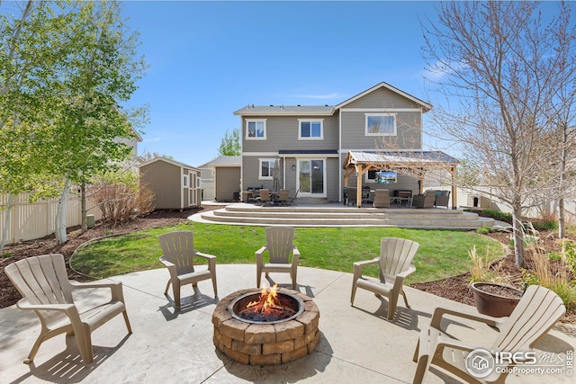 rear view of house with a shed, a deck, fence private yard, a fire pit, and an outbuilding