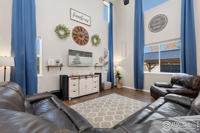living area featuring baseboards, a towering ceiling, and dark wood-style flooring