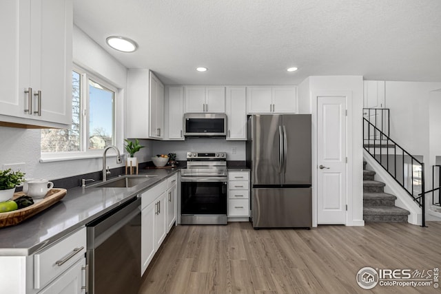 kitchen featuring a sink, stainless steel appliances, light wood finished floors, white cabinets, and recessed lighting