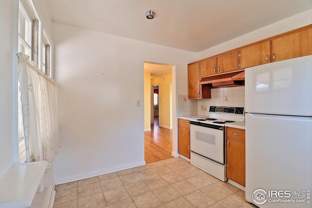 kitchen featuring decorative backsplash, white appliances, brown cabinets, light countertops, and under cabinet range hood