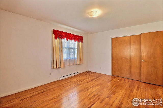 unfurnished bedroom featuring baseboard heating, baseboards, wood finished floors, and a closet
