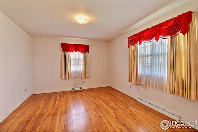 spare room with baseboard heating, visible vents, wood finished floors, and baseboards
