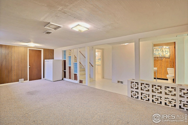 finished basement with wooden walls, carpet floors, visible vents, and stairs