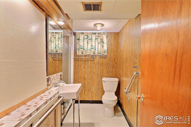 full bathroom with wood walls, a sink, a shower with curtain, toilet, and visible vents