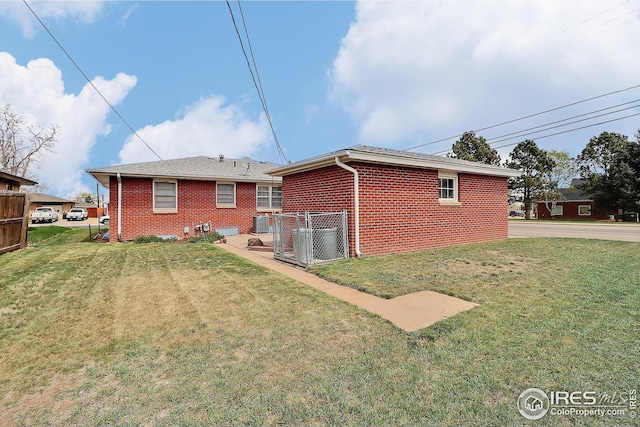 rear view of property featuring fence, a yard, and brick siding