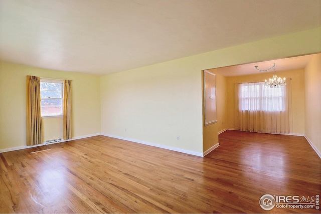 unfurnished room featuring an inviting chandelier, a wealth of natural light, and wood finished floors