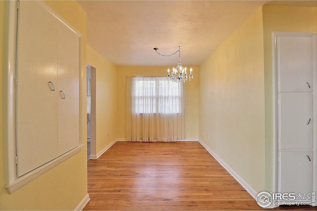 unfurnished dining area featuring an inviting chandelier, light wood finished floors, and baseboards