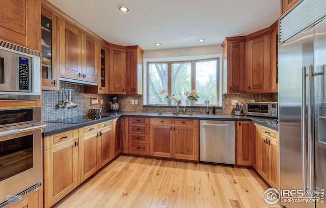 kitchen with light wood finished floors, a sink, tasteful backsplash, built in appliances, and brown cabinets
