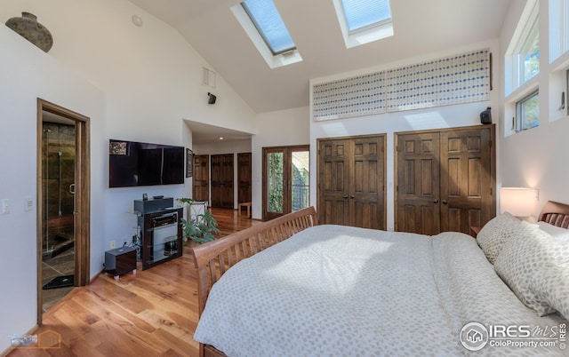 bedroom featuring a skylight, light wood-style flooring, high vaulted ceiling, and two closets