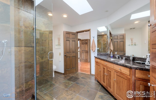 bathroom featuring a shower stall, toilet, vanity, and a skylight