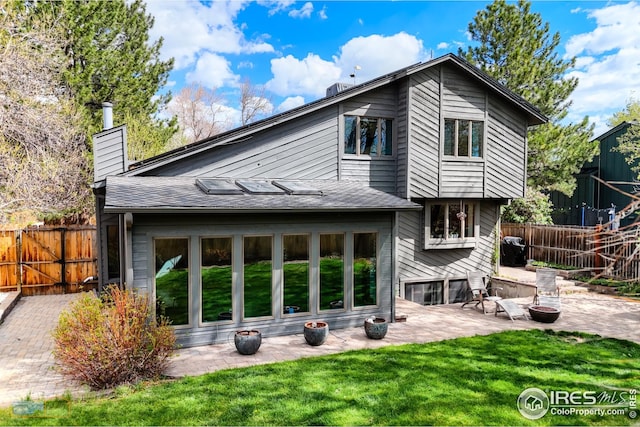 back of property featuring a patio area, a chimney, a lawn, a fenced backyard, and roof mounted solar panels