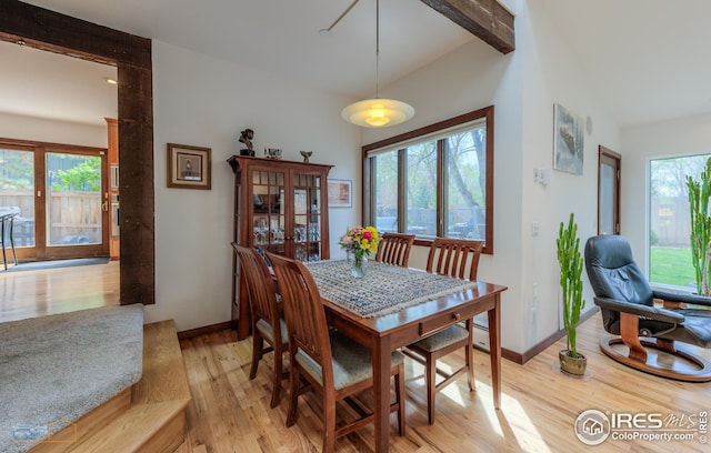 dining area featuring light wood finished floors, vaulted ceiling with beams, and baseboards