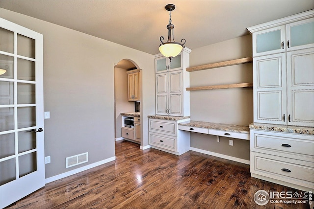 unfurnished office with visible vents, built in study area, baseboards, arched walkways, and dark wood finished floors