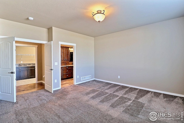 unfurnished bedroom with dark carpet, visible vents, ensuite bath, and baseboards