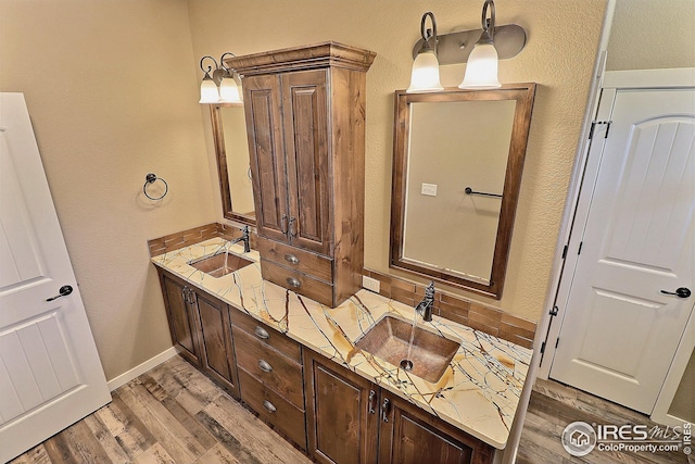 full bath featuring double vanity, wood finished floors, baseboards, and a sink