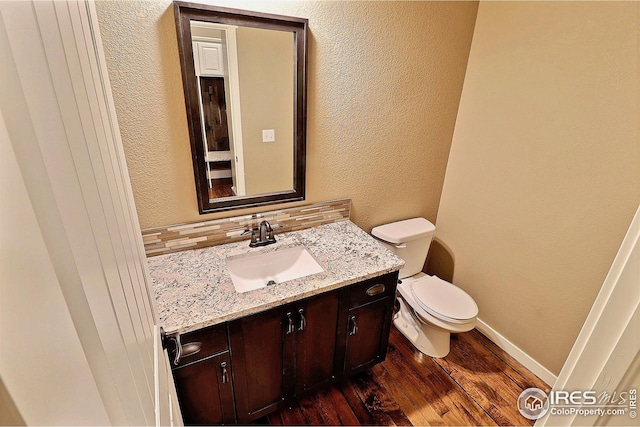 half bath with vanity, toilet, a textured wall, baseboards, and wood finished floors